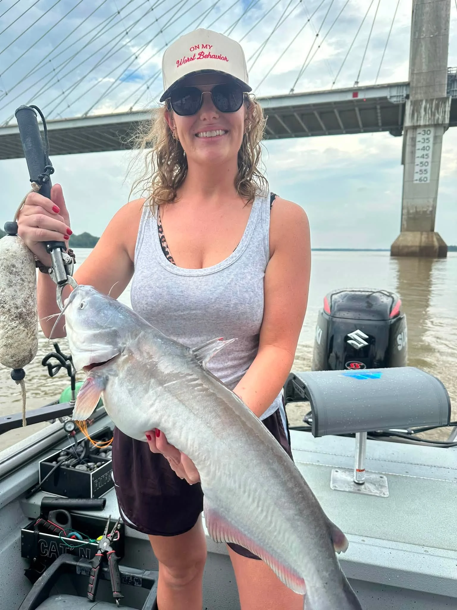 A smiling guest holding a large catfish near the river bridge