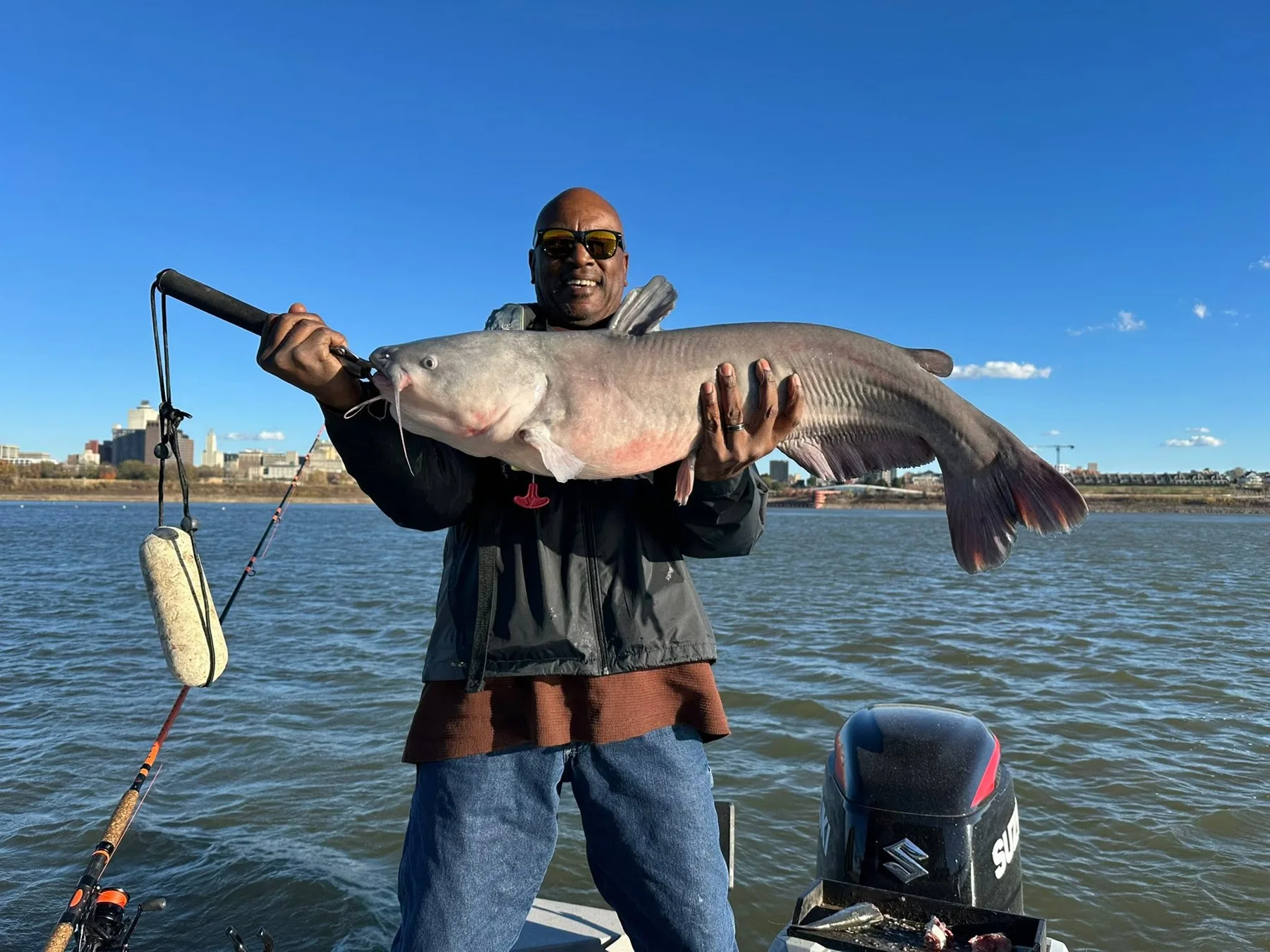 An angler holding a blue catfish against a bright sky