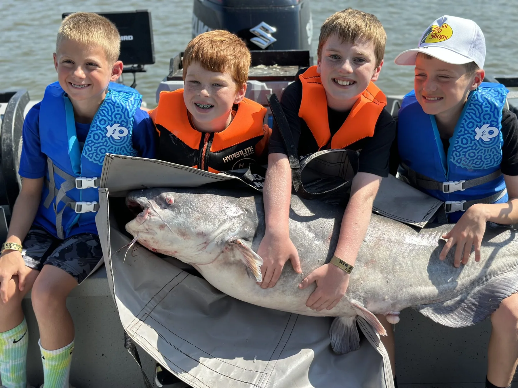 Four young anglers in life jackets holding a huge catfish aboard Captain Dave’s boat